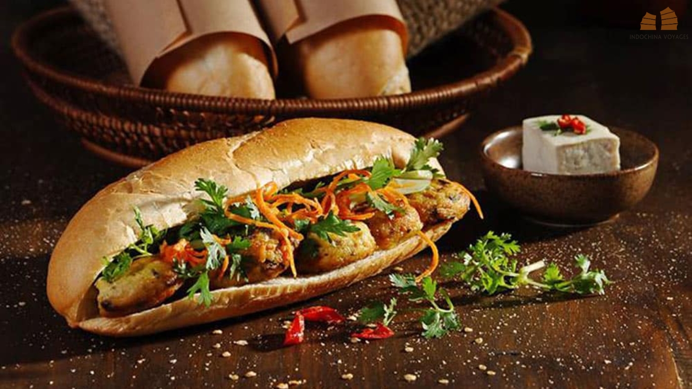 Banh mi baguette filled with grilled patties, pickled carrot and fresh herbs on a wooden table in Hanoi