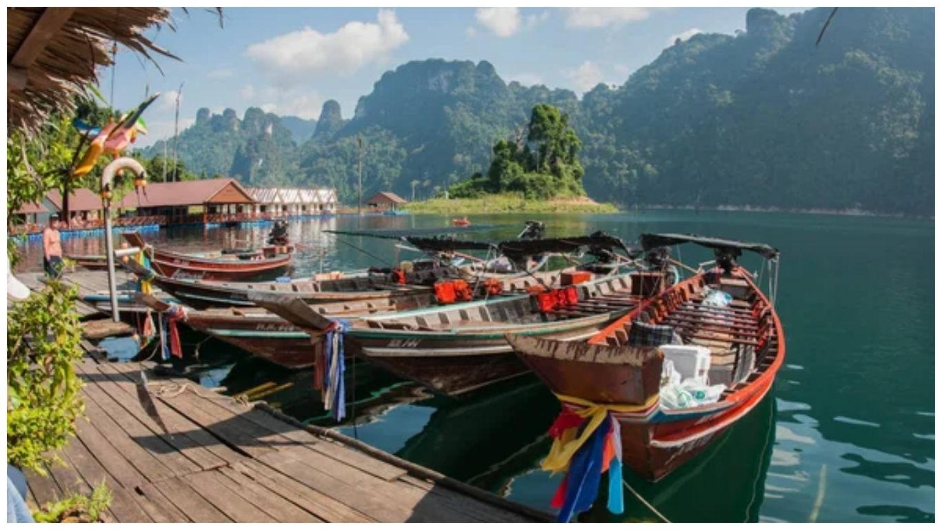 Scenic view of a boat pier in Thailand featuring traditional wooden boats and mountain landscapes under clear January skies.