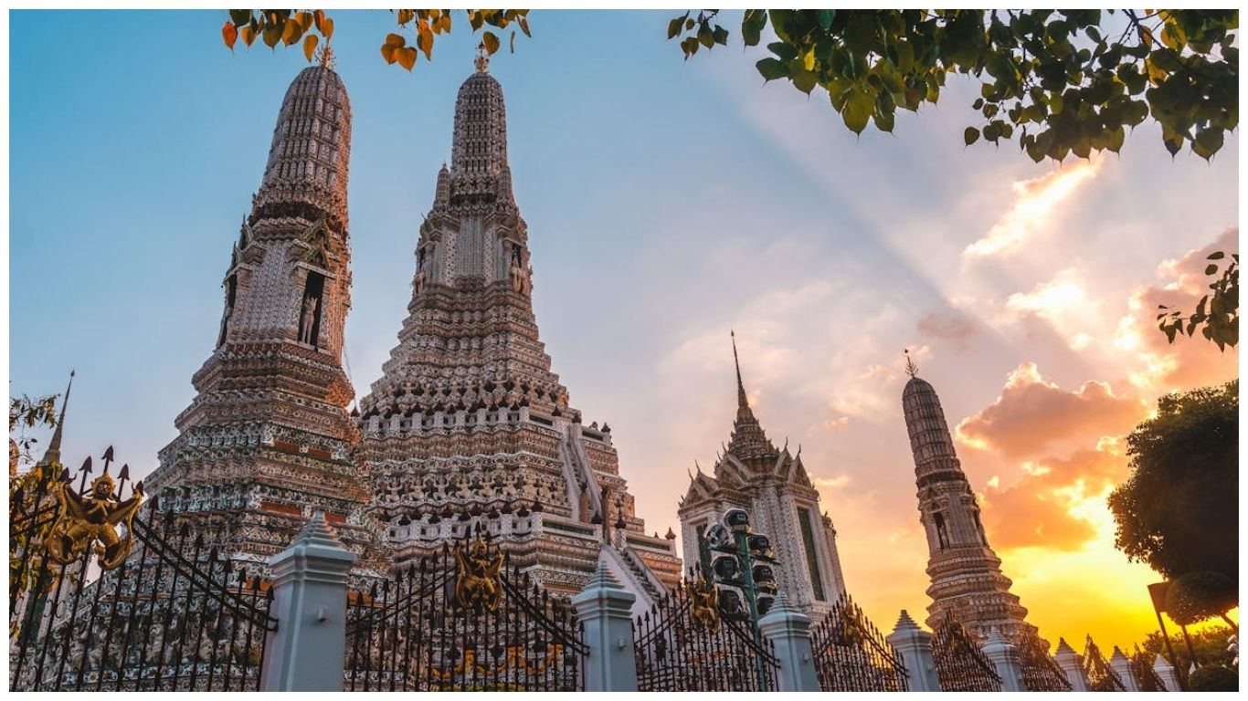Wat Arun temple in Bangkok, Thailand in June at sunset with golden sunlight hitting the white porcelain prangs