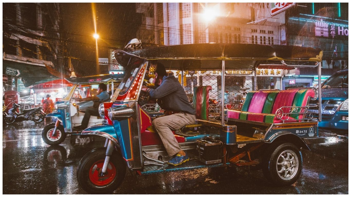 Colorful tuk-tuks parked on a rainy street in Bangkok, Thailand during the August monsoon season at night