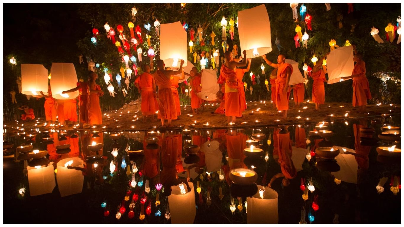 Buddhist monks releasing glowing paper lanterns at night in Thailand in November during Loy Krathong festival