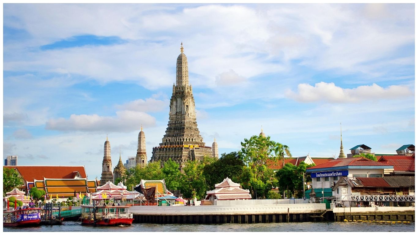 The iconic central prang of Wat Arun (Temple of Dawn) standing tall against a blue sky with white clouds in Bangkok, Thailand