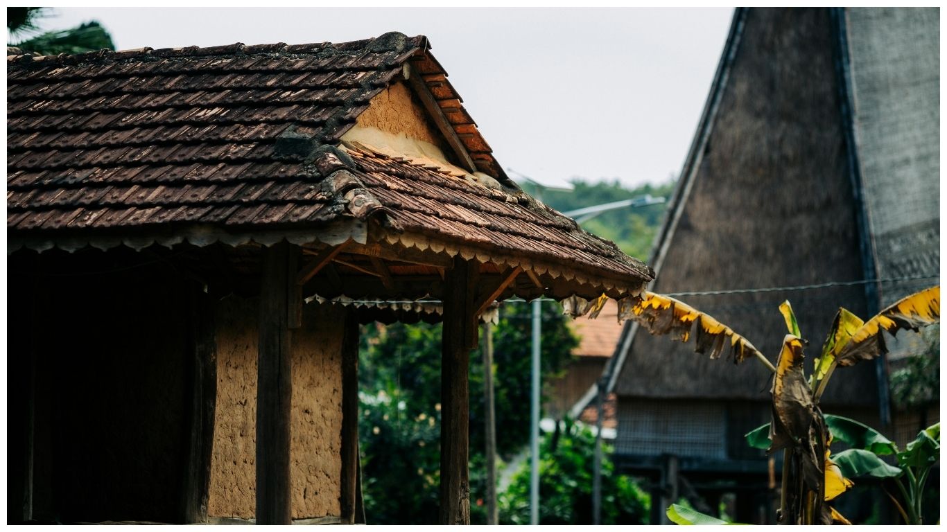 Close-up of a traditional Thai wooden house with a tiled roof surrounded by lush green trees and banana plants in Phuket, Thailand