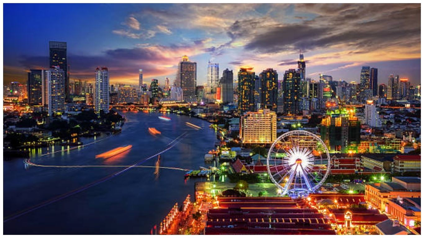 A panoramic sunset view of the Bangkok skyline and Chao Phraya River with a ferris wheel at Asiatique, perfect for a trip to Thailand in November