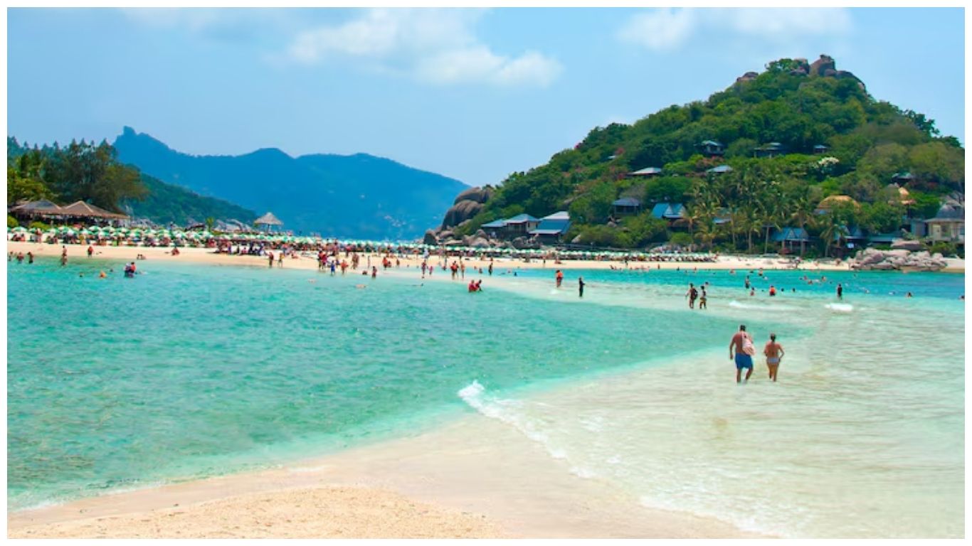 Tourists walking on the white sandbar connecting islands at Pattaya in Thailand in November under a clear blue sky
