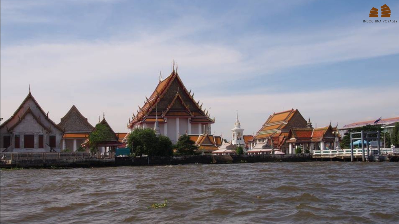 Thonburi riverside temple with orange tiled roofs seen from a boat on the Chao Phraya River