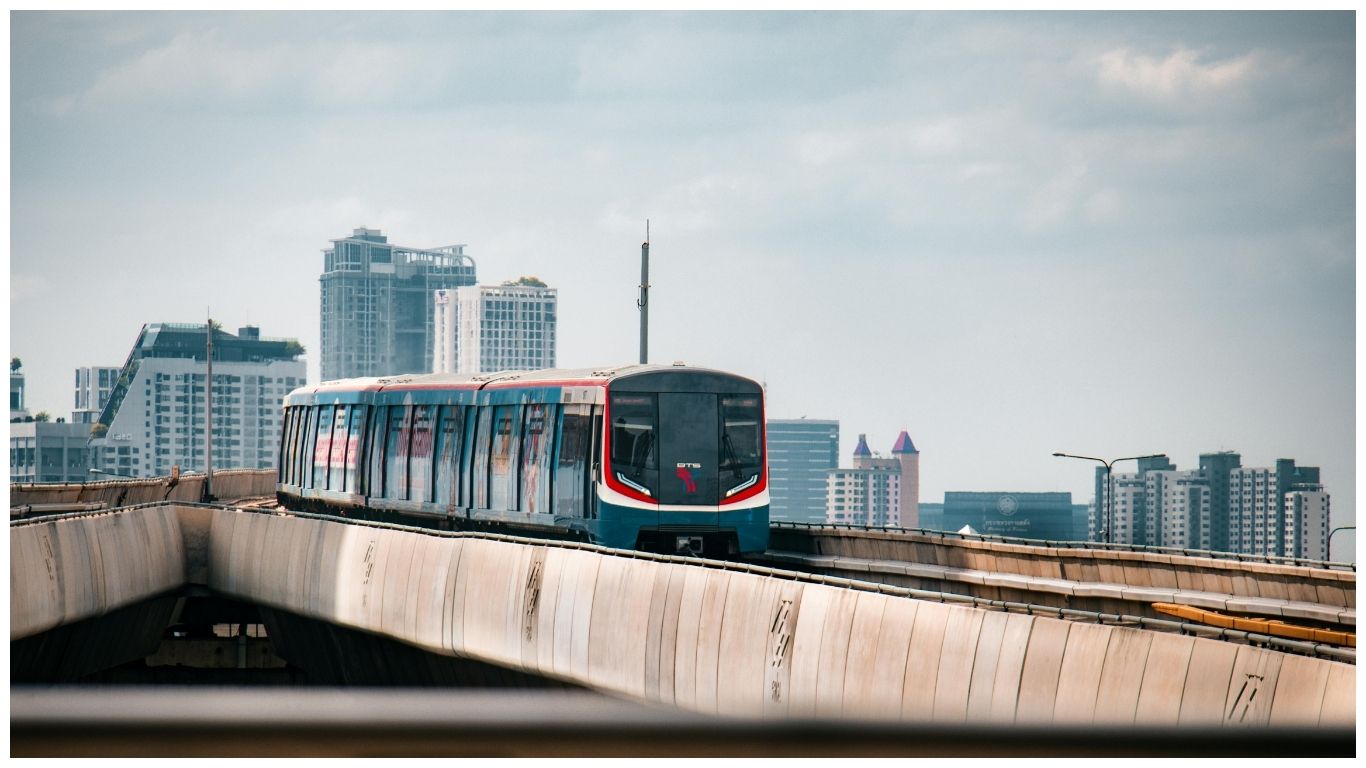 A modern BTS Bangkok Skytrain traveling on an elevated track against a backdrop of city skyscrapers and a clear sky in Bangkok, Thailand