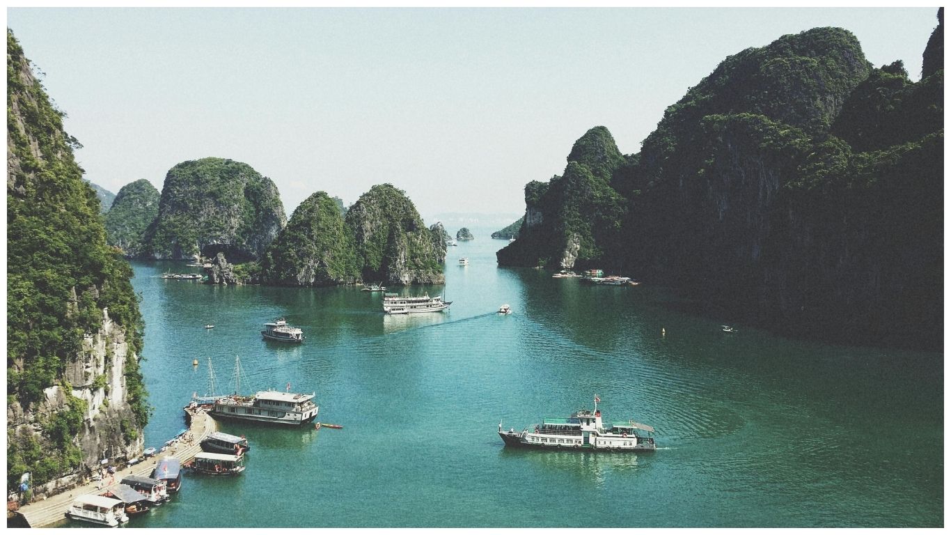 A scenic view of Ha Long Bay featuring several cruise boats sailing between towering limestone karsts in the emerald waters of Vietnam.