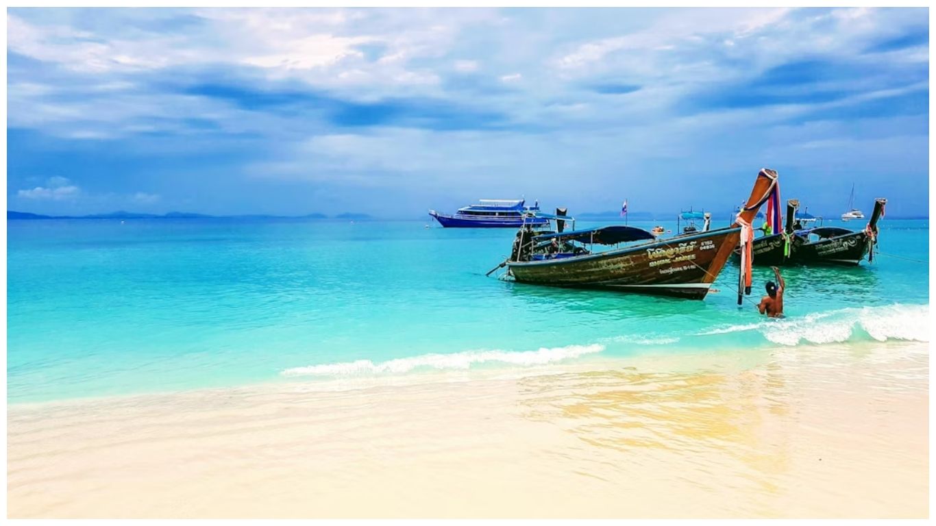 Traditional Thai long-tail boats anchored on a white sand beach with turquoise water in Phuket, one of the best places to visit in Thailand