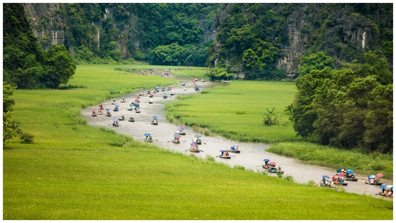 Traditional wooden boats traveling through the lush green rice fields and limestone mountains of Tam Coc, one of the best day trips from Hanoi, Vietnam