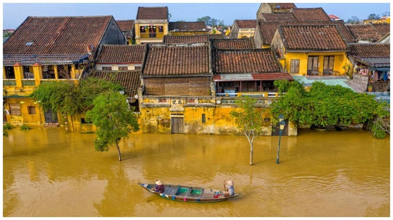 Aerial view of flooded yellow ancient houses in Hoi An during the rainy season with a small wooden boat navigating the submerged streets of Vietnam