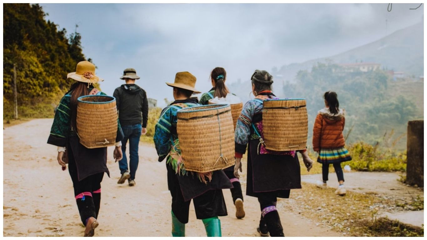 A group of local ethnic minority people with traditional woven baskets walking alongside a traveler on a mountain path in Sapa, Vietnam