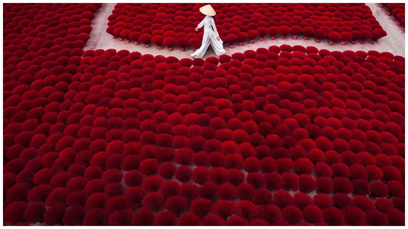 A person wearing a traditional Ao Dai walks through red incense bundles at Quang Phu Cau incense village, one of the best day trips from Hanoi, Vietnam