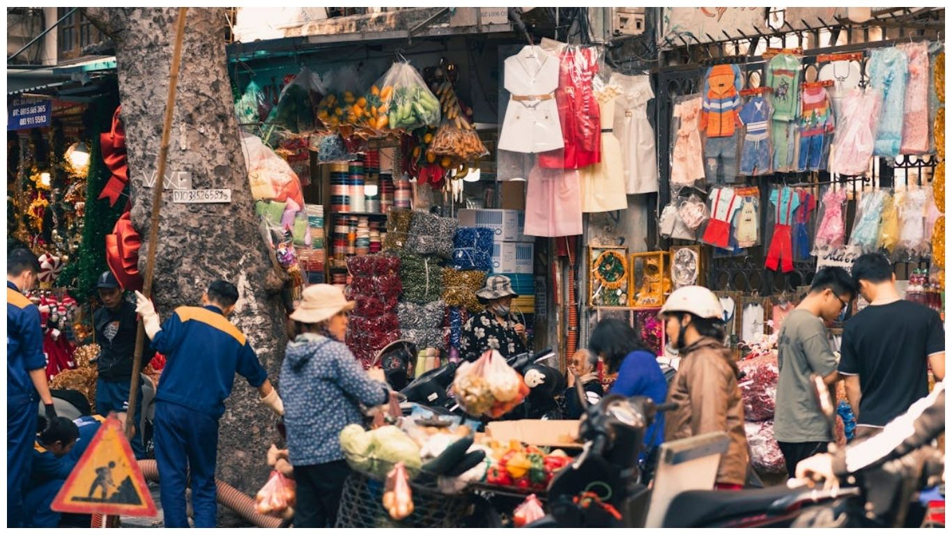 A vibrant and crowded local street market in the Hanoi Old Quarter, showing vendors selling clothes and fresh produce, perfect for those deciding between Hanoi or Bangkok
