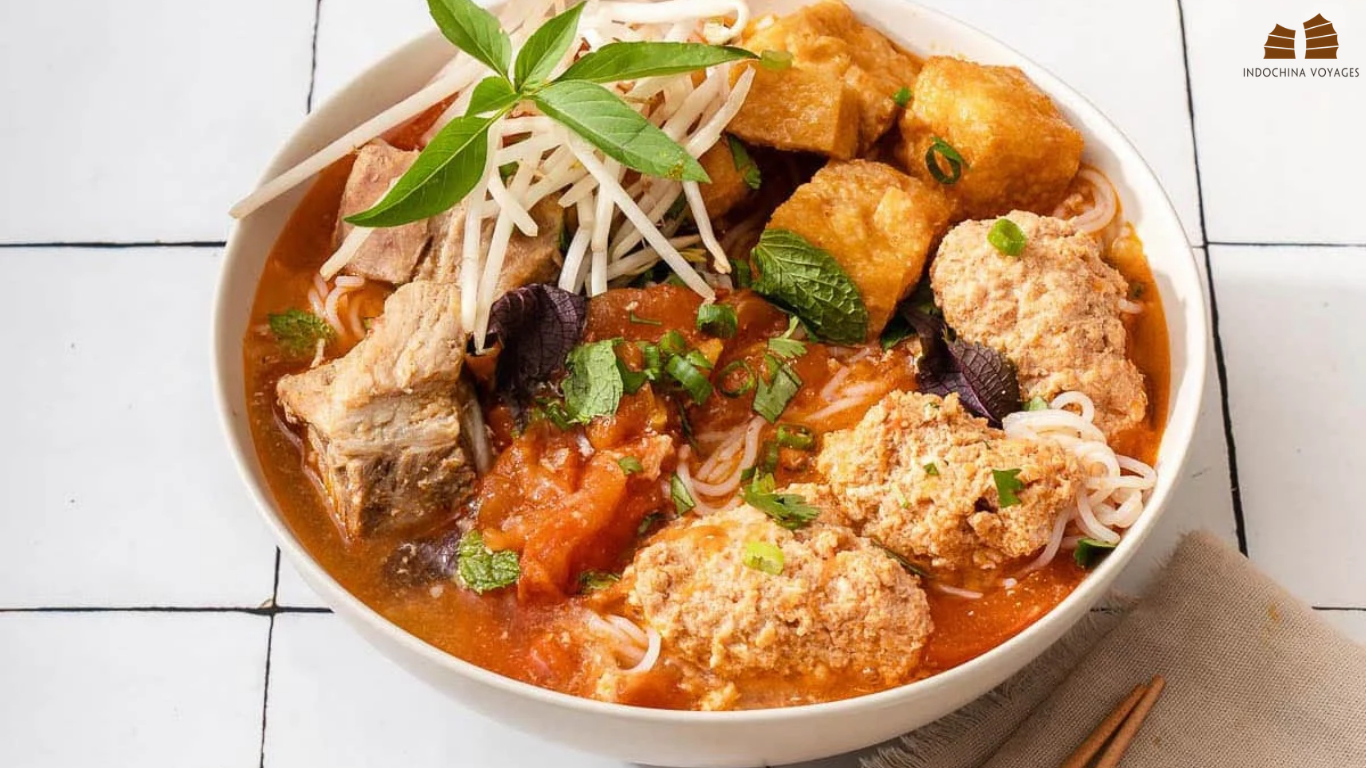 Bowl of bun rieu crab noodle soup with tomato broth, fried tofu, pork and fresh herbs in Hanoi