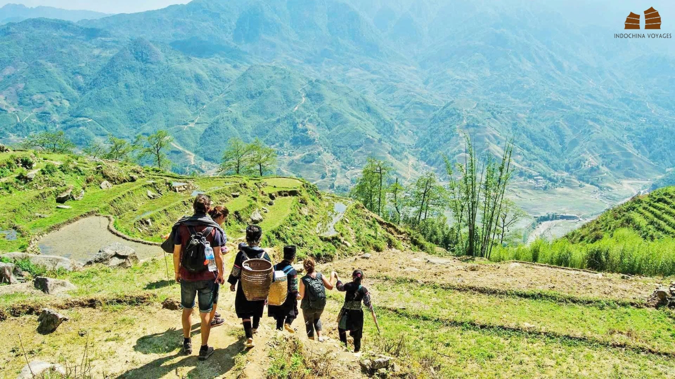 Trekkers and local guides descending a terraced hillside above a wide mountain valley, Sapa