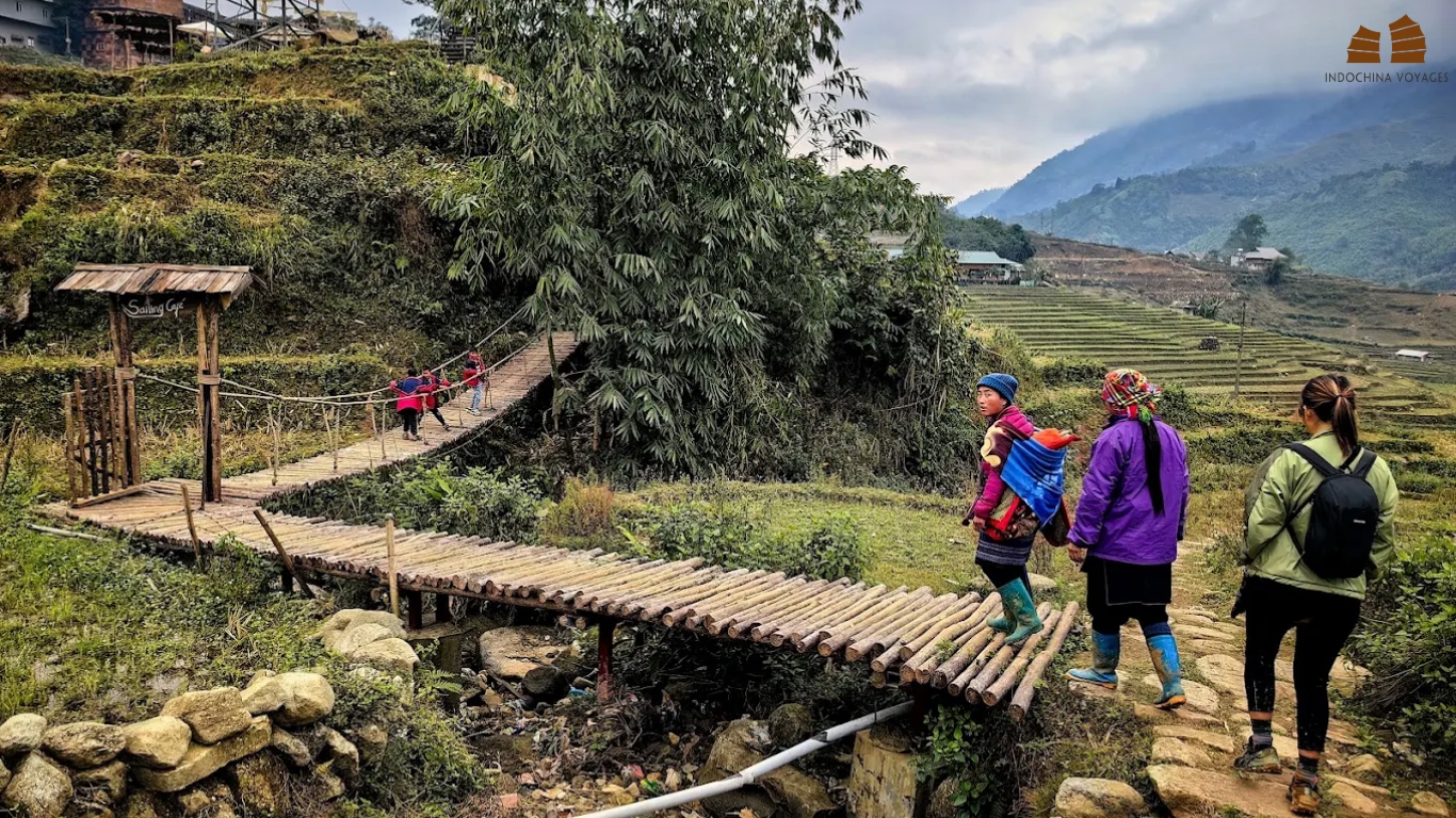 Trekker and villagers on a bamboo footbridge beside rice terraces in a Sapa valley
